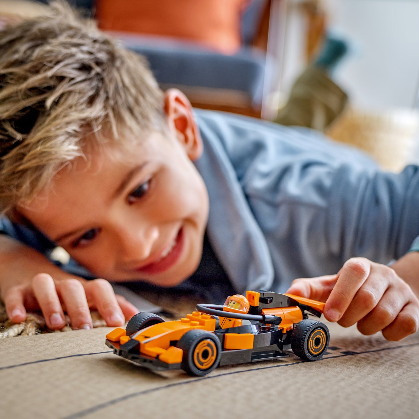 Child playing with LEGO City F1 Driver with McLaren Race Car set and the assembled orange and black race car model with a minifig driver.