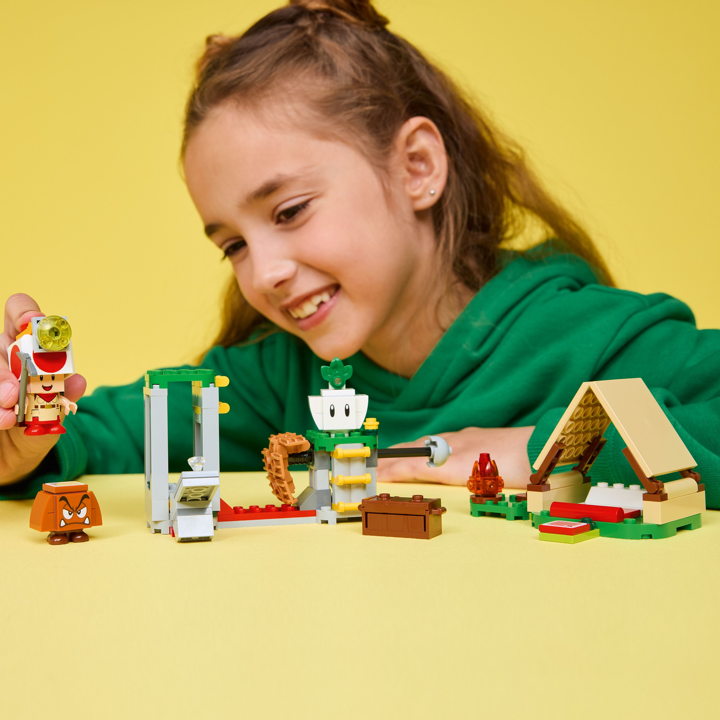 Child playing with LEGO Super Mario set with packaging, characters, and structures on a white background