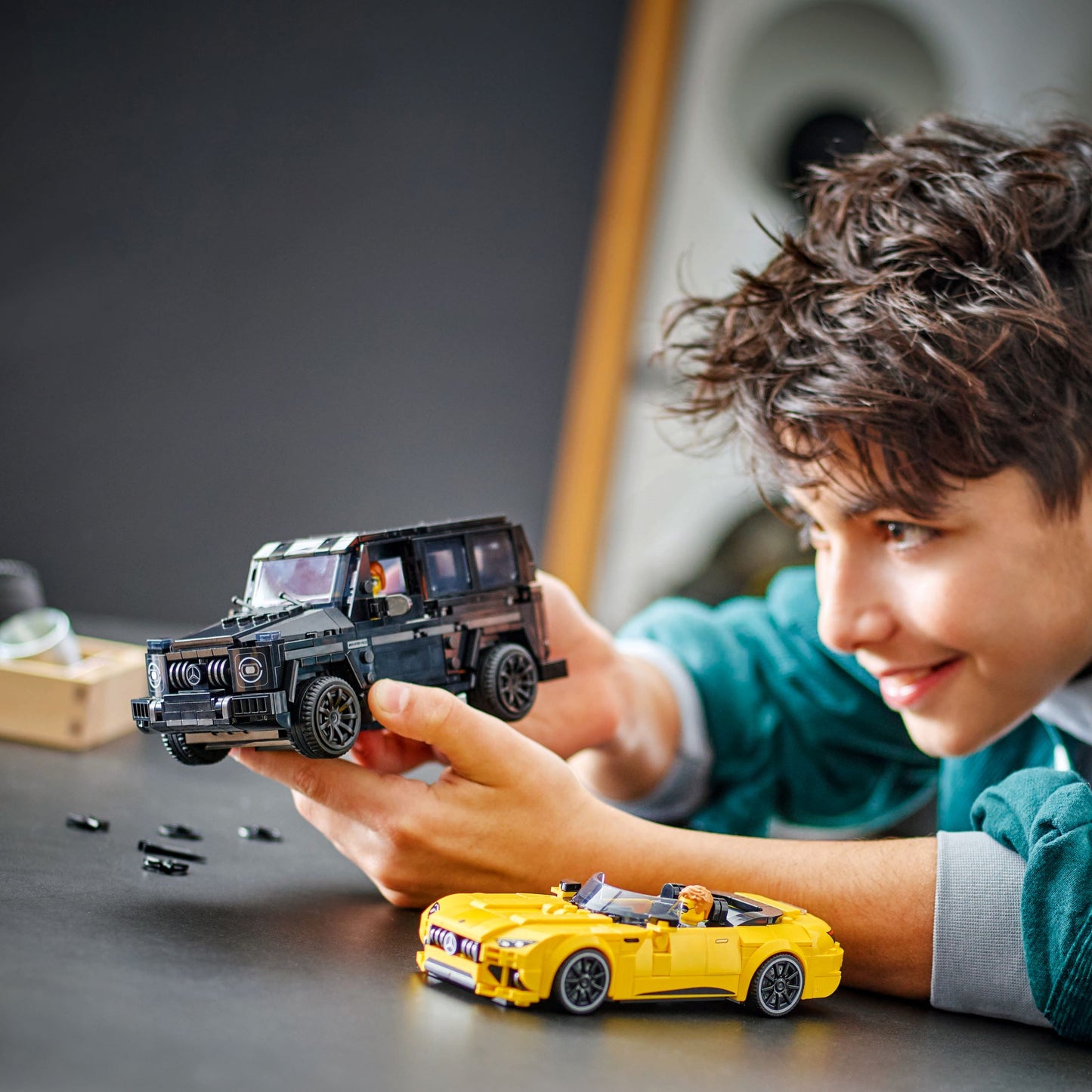 Child playing with LEGO Speed Champions set featuring models of Mercedes-AMG G63 and Mercedes-AMG SL63 on a table.
