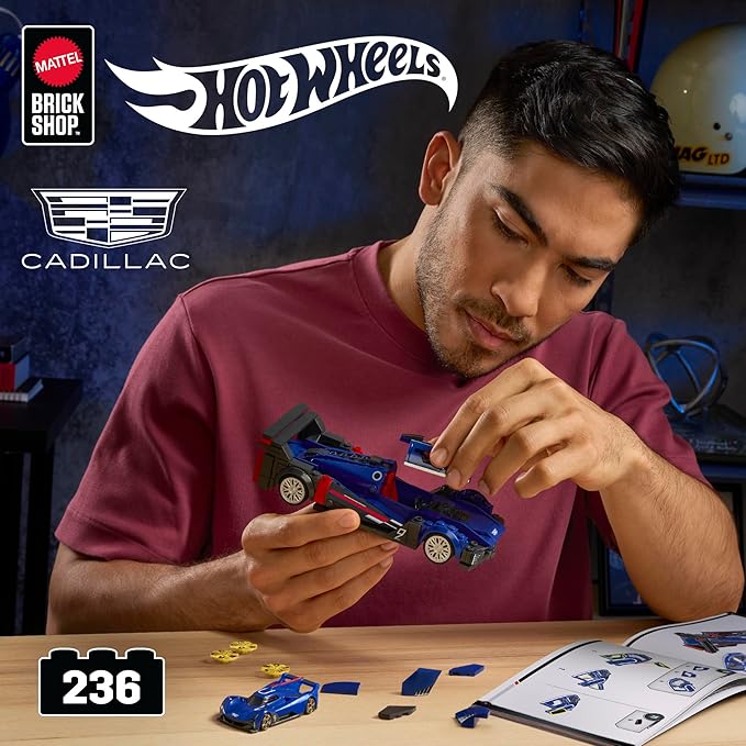 Man playing with a Hot Wheels toy car in a garage setting with Cadillac branding.