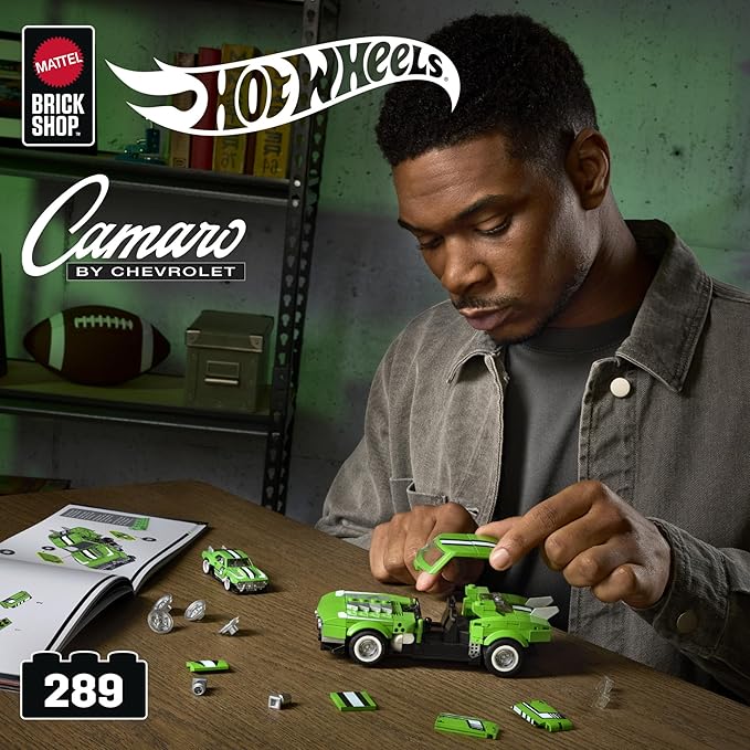 Man playing with Hot Wheels toy cars on a table, with 'Hot Wheels' and 'Brick Shop' branding visible.
