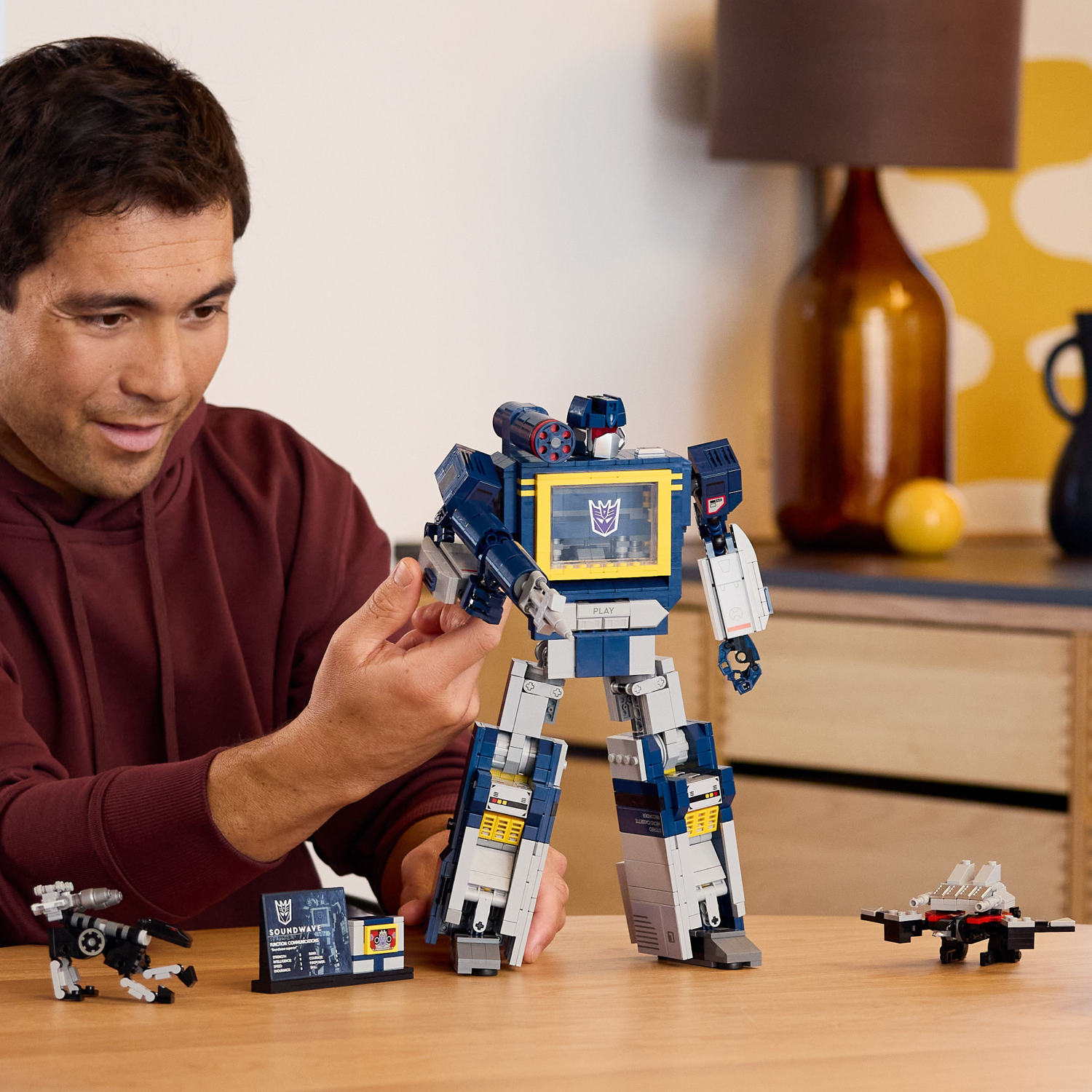 Man playing with a LEGO Transformers Soundwave robot toy on a table.