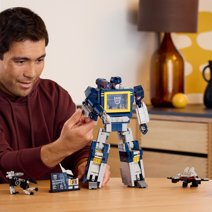 Man playing with a LEGO Transformers Soundwave robot toy on a table.