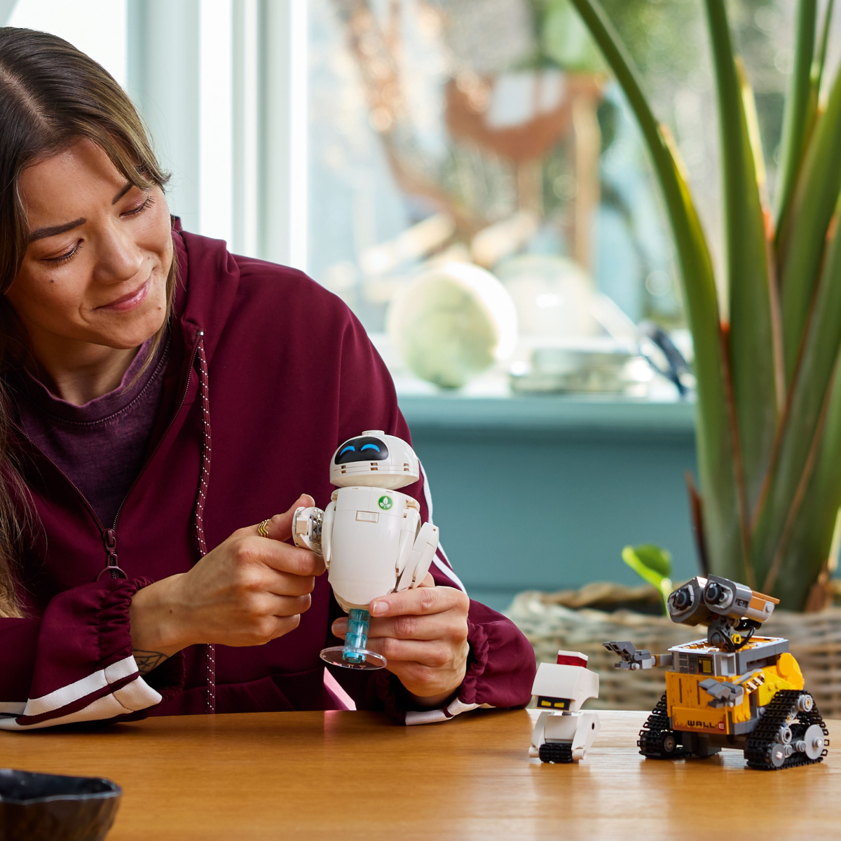 Woman Playing with Two robot LEGO toys, one resembling WALL-E and the other resembling EVE from 'EVE,' on a wooden table.