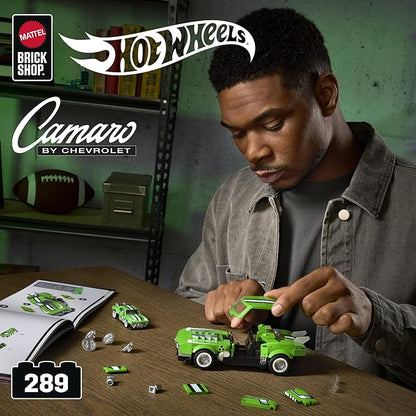 Man playing with Hot Wheels toy cars on a table, with 'Hot Wheels' and 'Brick Shop' branding visible.